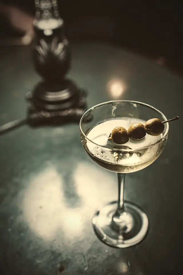 A dirty martini with three olives on a dark marble bar top.