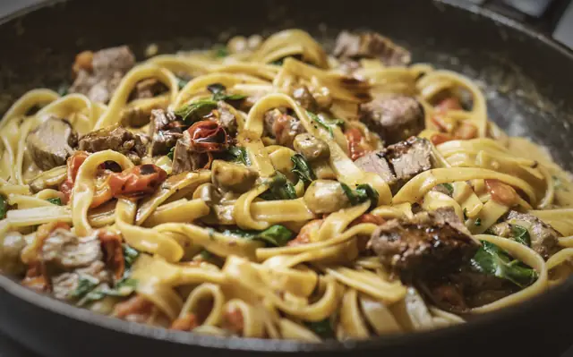 Ribbons of fresh pasta tossed with braised meat and greens in a black pan.