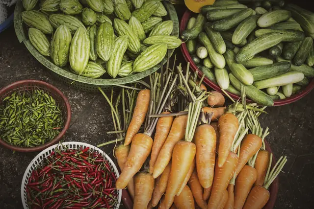 Baskets of carrots, cucumbers, bitter melon and red chiles at a farm stand.