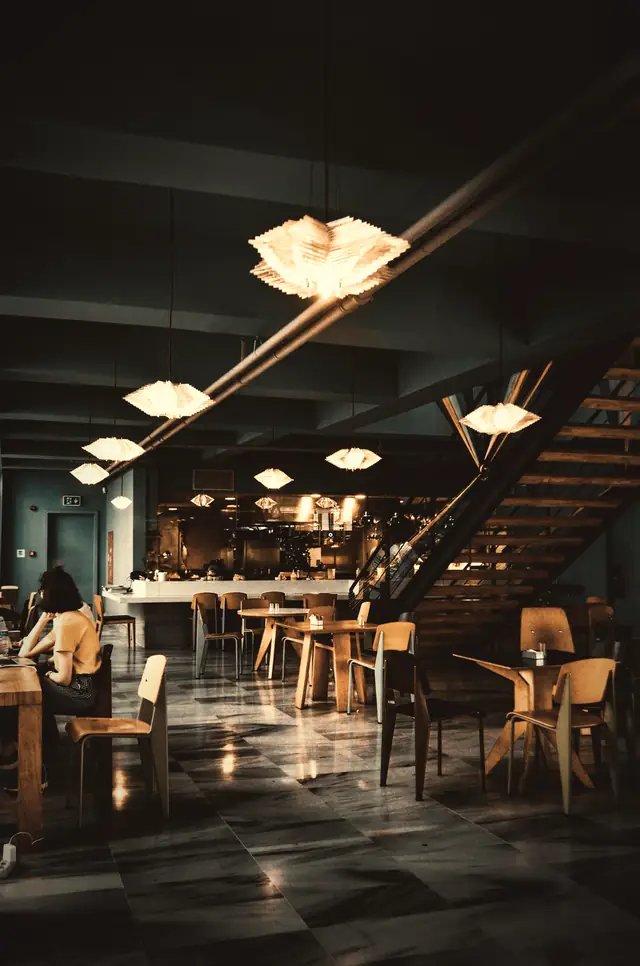 A dim dining room with pendant lights and a staircase to a mezzanine.