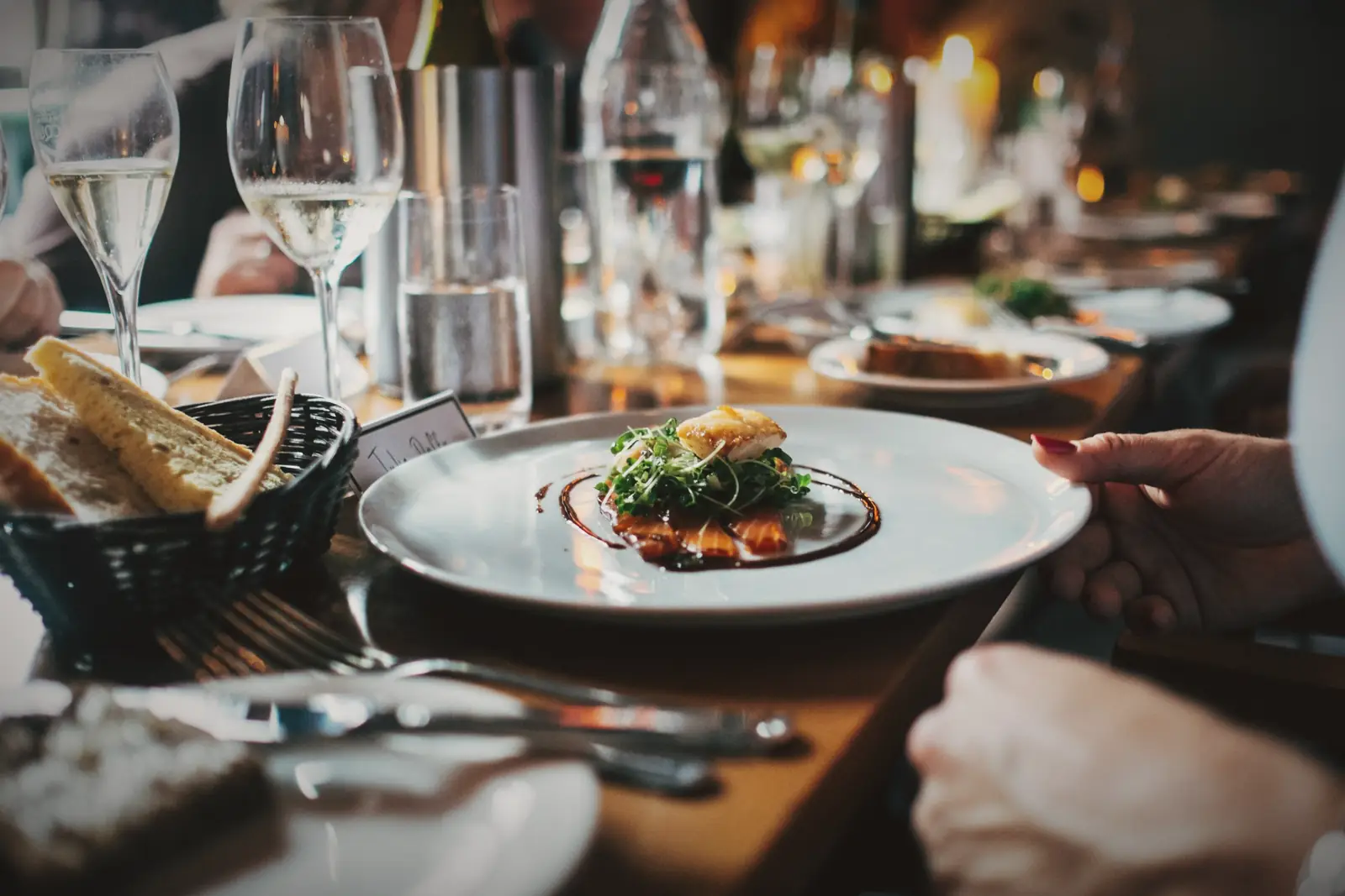 A candlelit table set with wine glasses as a plate is served.