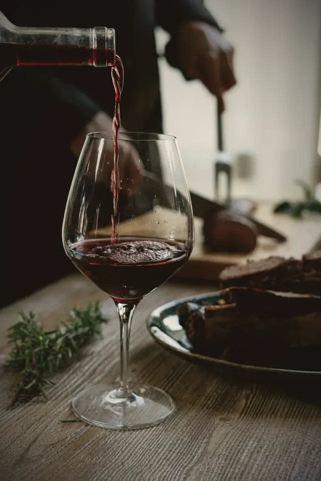 Red wine being poured into a glass beside a carving board.